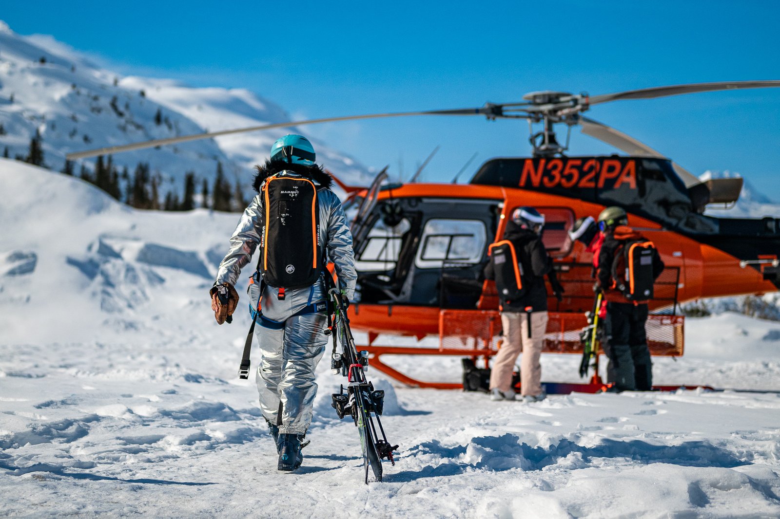 Heli-skier walking toward a helicopter ready for takeoff in the Chugach Mountains, Alaska